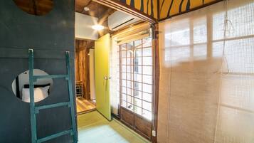 A traditional Japanese room with tatami flooring, a sliding door, and a ladder leading to a loft bed.