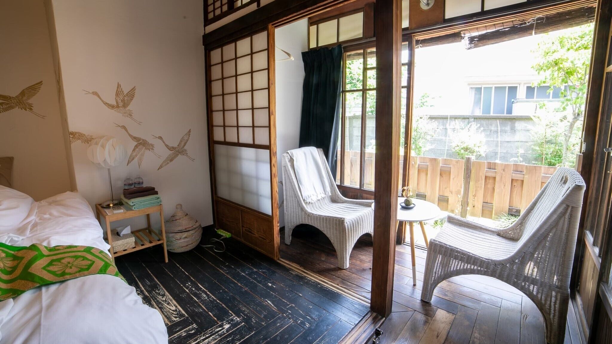 Ein traditioneller japanischer Raum mit Tatami-Boden, einer verschiebbaren Shoji-Schirmwand, einem Bett mit einer grün gemusterten Decke und Blick ins Freie.