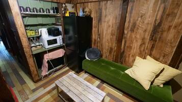 A cozy room with a green sofa, a wooden floor, a small table, and a kitchenette area with a microwave and coffee maker.
