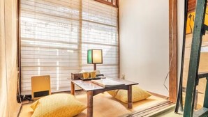 Um quarto japonês tradicional com tatames, uma mesa baixa com almofadas, um aquecedor e uma janela com divisórias de papel shoji.