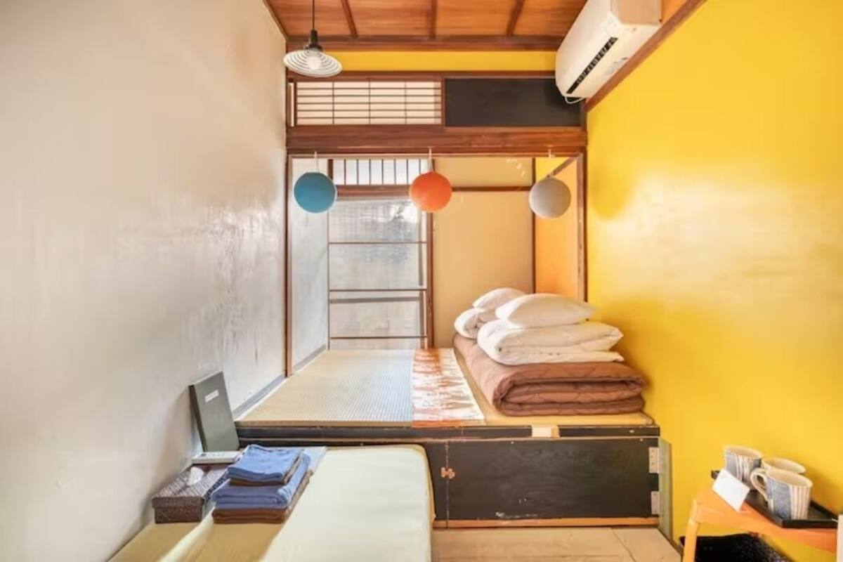 A traditional Japanese room with tatami flooring, a futon bed, a shoji screen, and a small table with a kettle and cups.