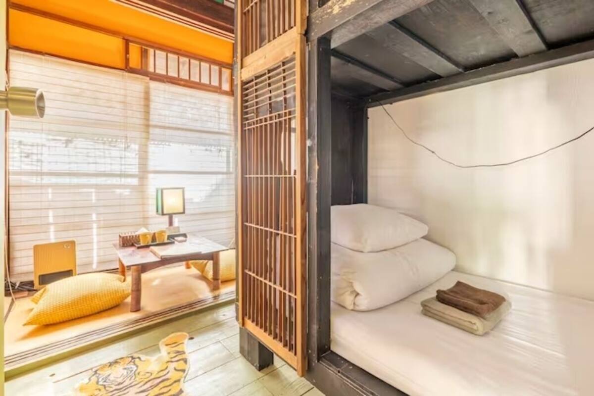 A traditional Japanese room with tatami flooring, a low wooden desk, a bed with pillows, and a sliding door.