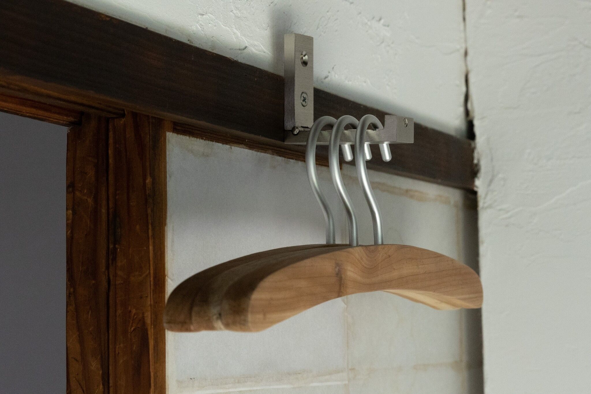 A wooden coat rack with metal hooks against a white wall.