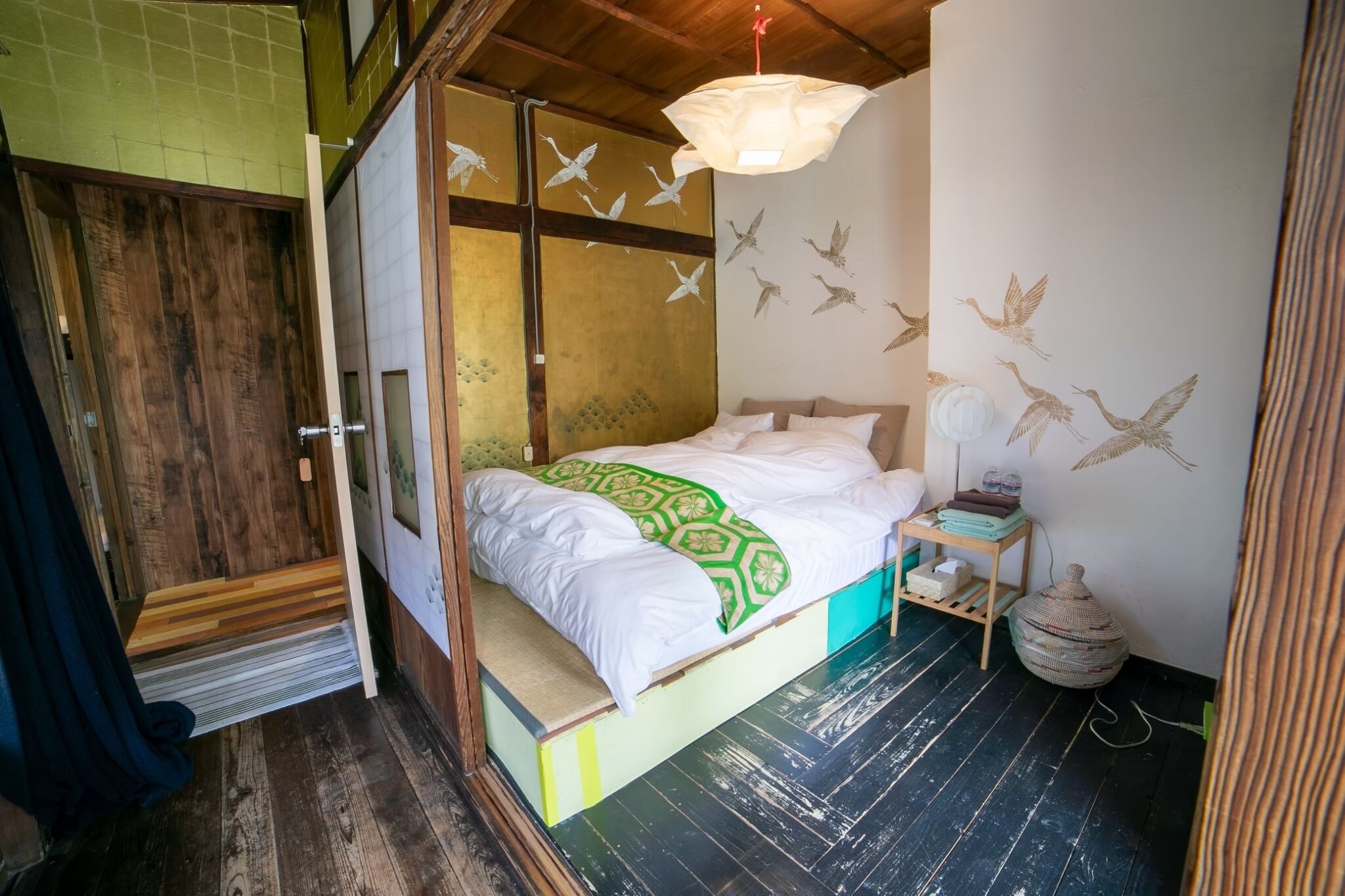 Um quarto com cama, piso de madeira, parede decorada com arte de aves e luminária pendente.