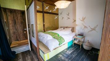 Um quarto com cama, piso de madeira, parede decorada com arte de aves e luminária pendente.