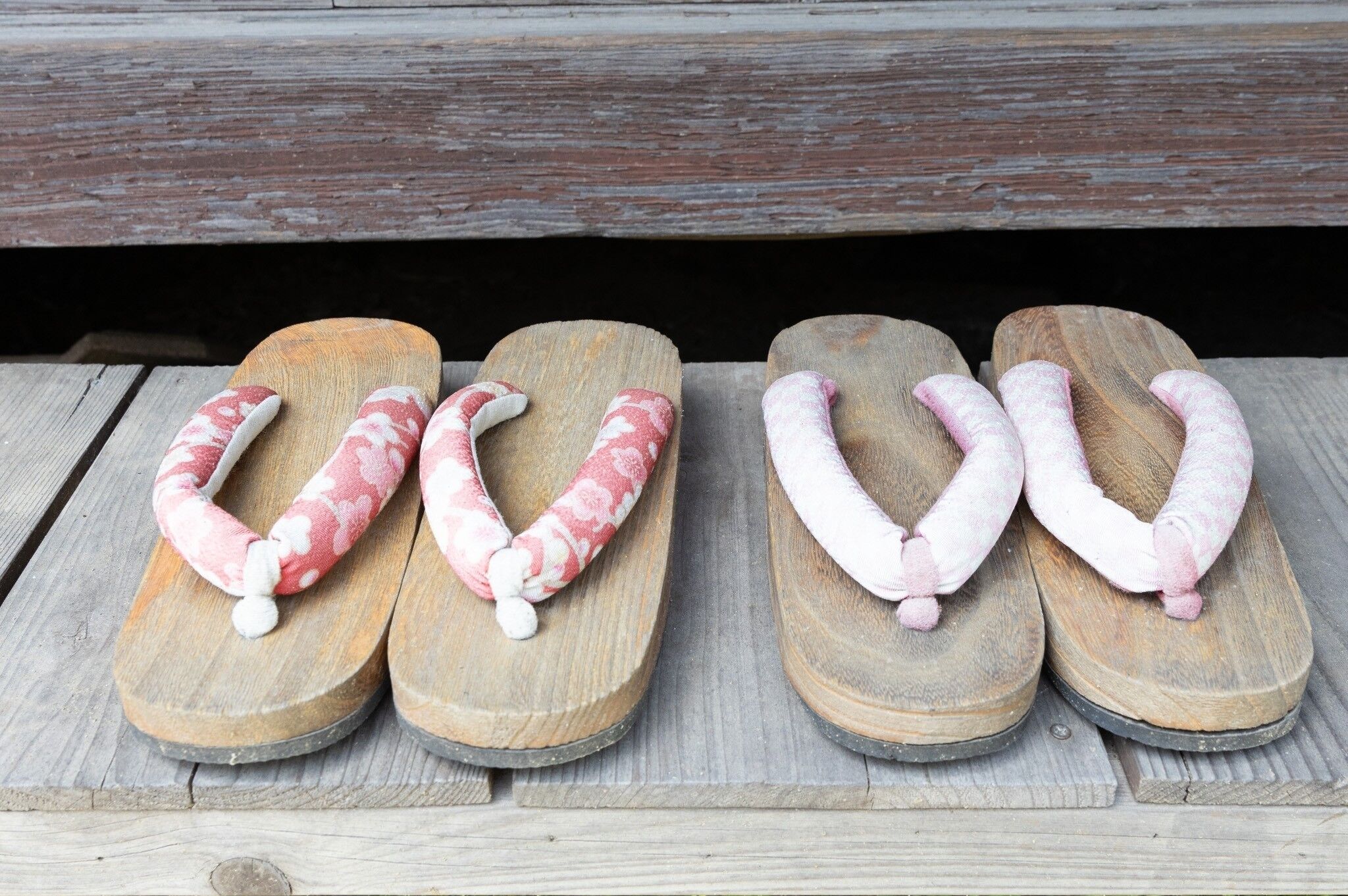 Four pairs of slippers with a pink and white pattern, placed on a wooden surface.