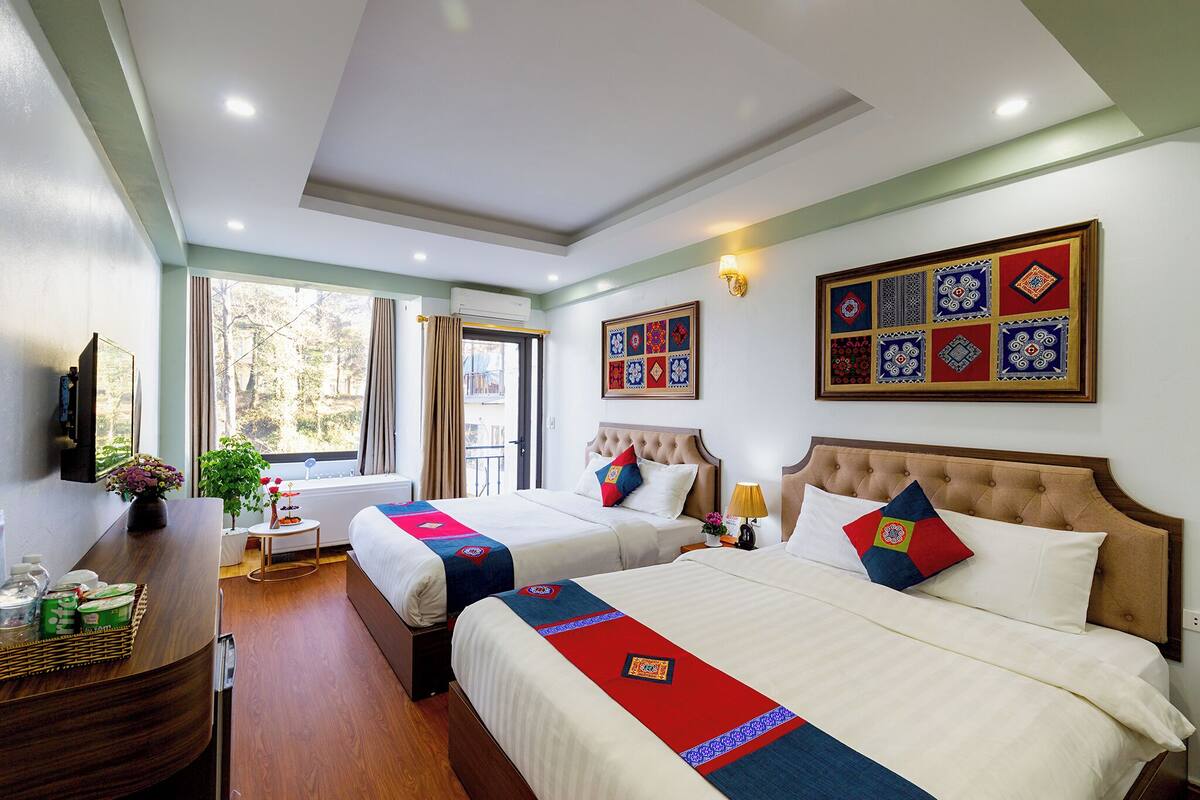 A hotel room with two beds, a TV, a desk with a basket of toiletries, and a window with curtains.
