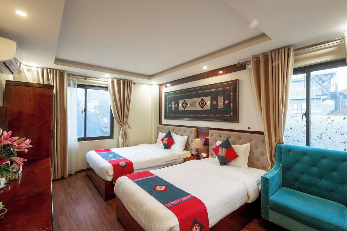 A hotel room with two beds, a large window, a sofa, and a decorative wall piece.