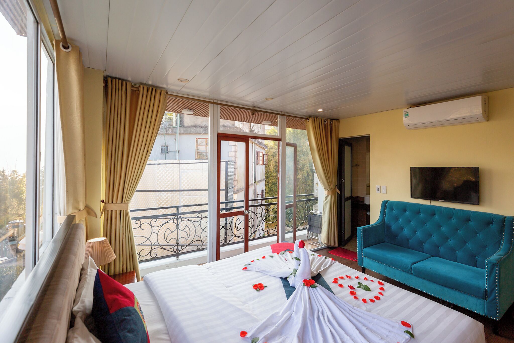 Una camera d'albergo con un letto, un divano blu, una televisione e un balcone con tende.