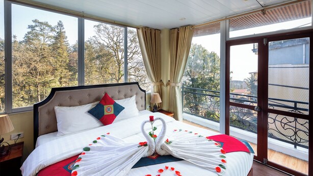 Une chambre d’hôtel avec un grand lit, une vue sur les arbres par les fenêtres et un balcon avec une balustrade.