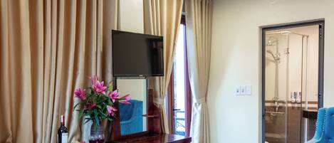 A hotel room with a wooden desk, a flat-screen TV, a vase with flowers, and a blue armchair.
