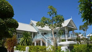 A large, multi-story building with a white facade and blue balconies, surrounded by lush greenery. - Moon Margo (Cha-am)