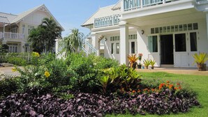 A two-story house with a balcony, surrounded by a well-maintained garden with various plants and flowers. - Moon Margo (Cha-am)