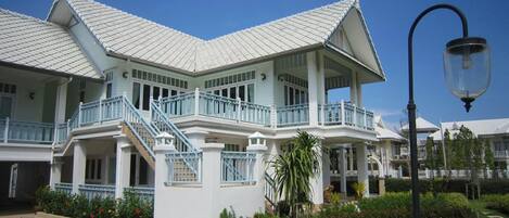A large, two-story building with a white facade and blue railings, featuring a central staircase and multiple balconies.