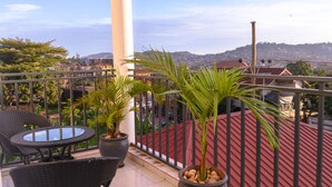 Un balcon agrémenté de meubles en osier, de plantes en pot et offrant une vue sur le paysage urbain et les collines.