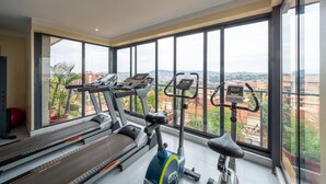 Une salle de sport équipée de tapis de course et de vélos d’appartement, avec de grandes fenêtres offrant une vue sur la ville.