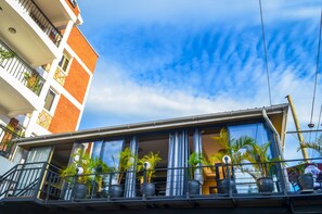 A hotel with a balcony with potted plants, a clear blue sky, and a multi-story building with red and white walls. - Dana Hotel (Kampala)