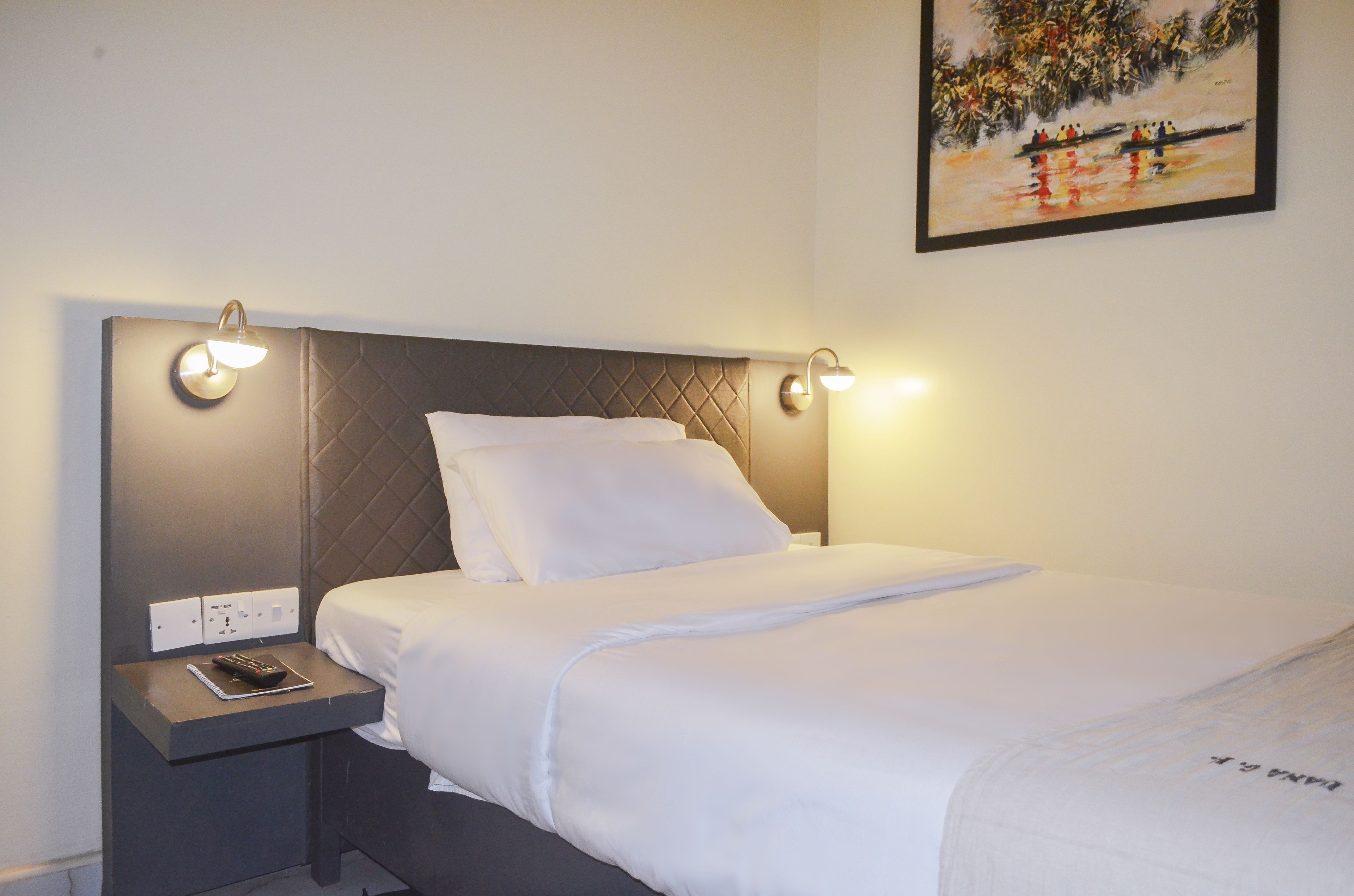 A neatly made bed with white linens, a headboard with a quilted pattern, and bedside lamps on either side.