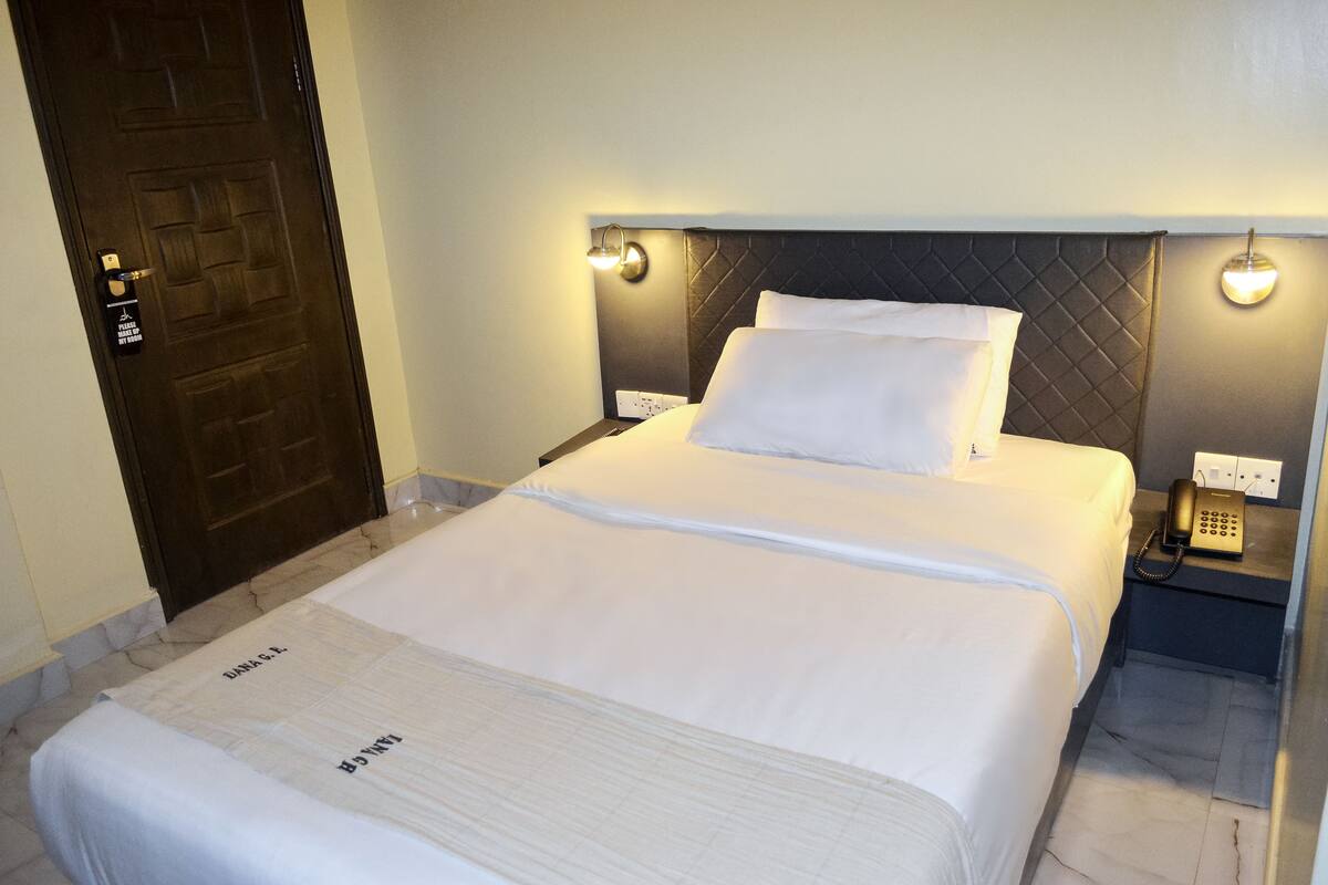 A neatly made bed with white linens, a dark headboard, and bedside lamps.