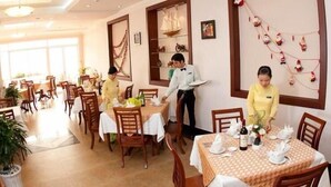 A dining area with tables set for service, a waiter attending to a table, and a decorative wall with ornaments. - Ocean Star Hotel (Ho Chi Minh City)