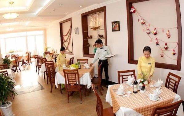 A dining area with tables set for service, a waiter attending to a table, and a decorative wall with ornaments.