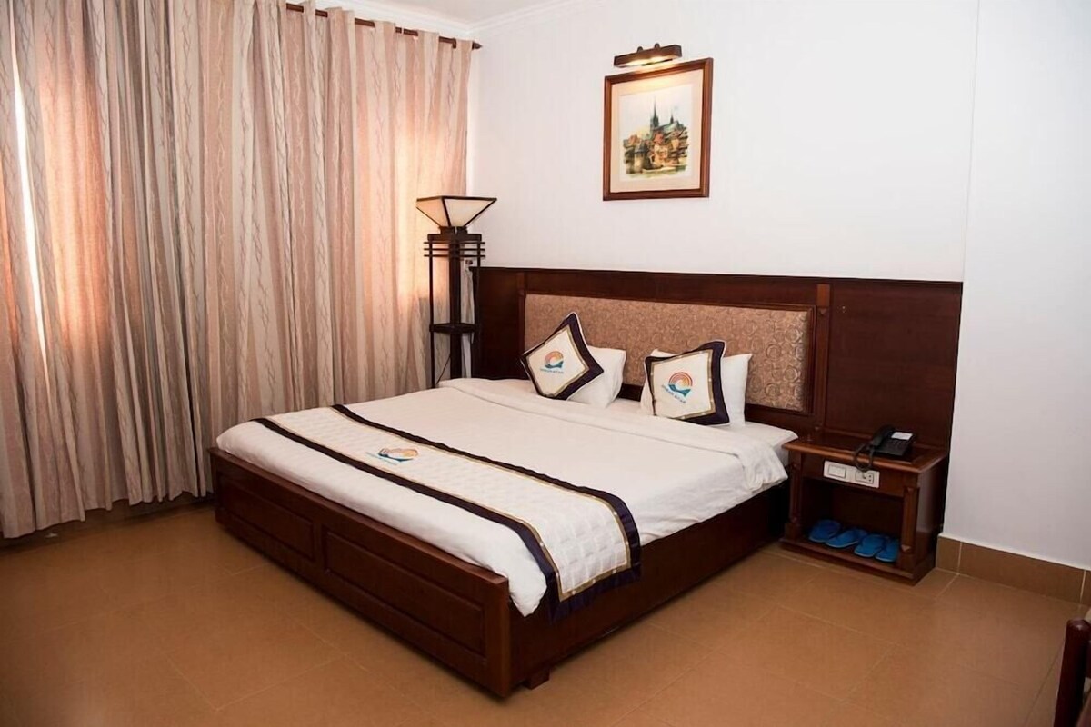 A hotel room with a large bed, a bedside table with a lamp, and a framed picture on the wall.