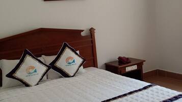 A neatly made bed with a quilted cover, two pillows with a logo, a bedside table with a phone, and a framed picture on the wall.