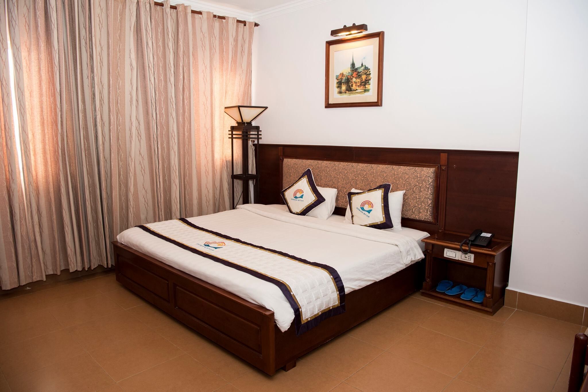 A hotel room with a large bed, a nightstand with a phone, and a lamp.