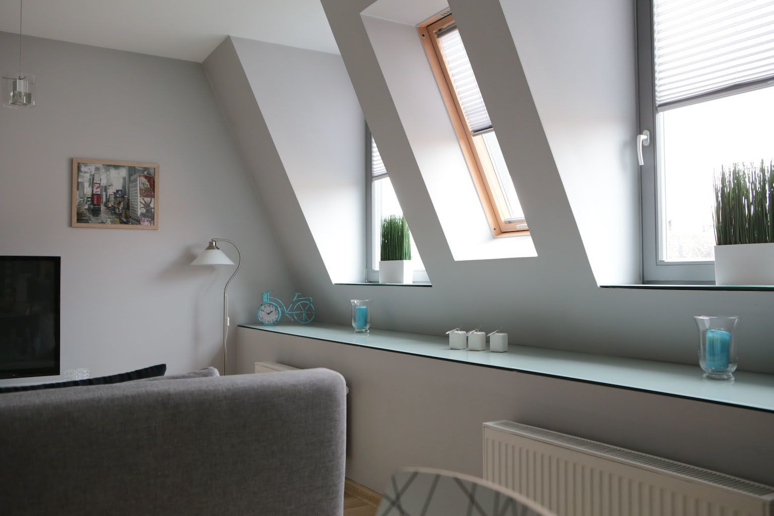 Un dormitorio tipo loft moderno con tragaluces, un cuadro de paisaje urbano, un escritorio con objetos decorativos y un radiador.