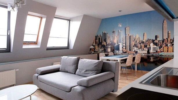 Un apartamento moderno con kitchenette, un sofá gris y un mural con vista a la ciudad.