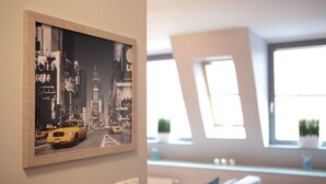 Una fotografía enmarcada de un paisaje urbano en una pared, una ventana con vista a un edificio, e interruptor en la pared.