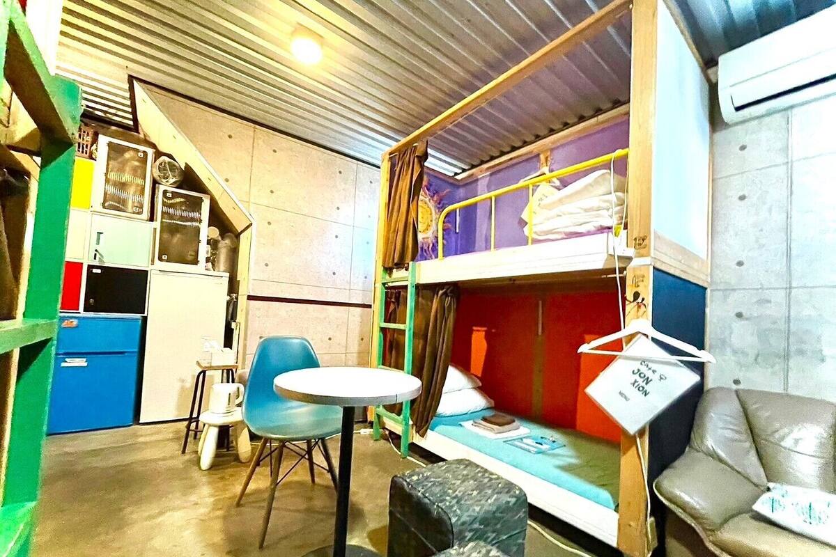 Habitación compacta con literas, una mesita, una silla y un sofá.