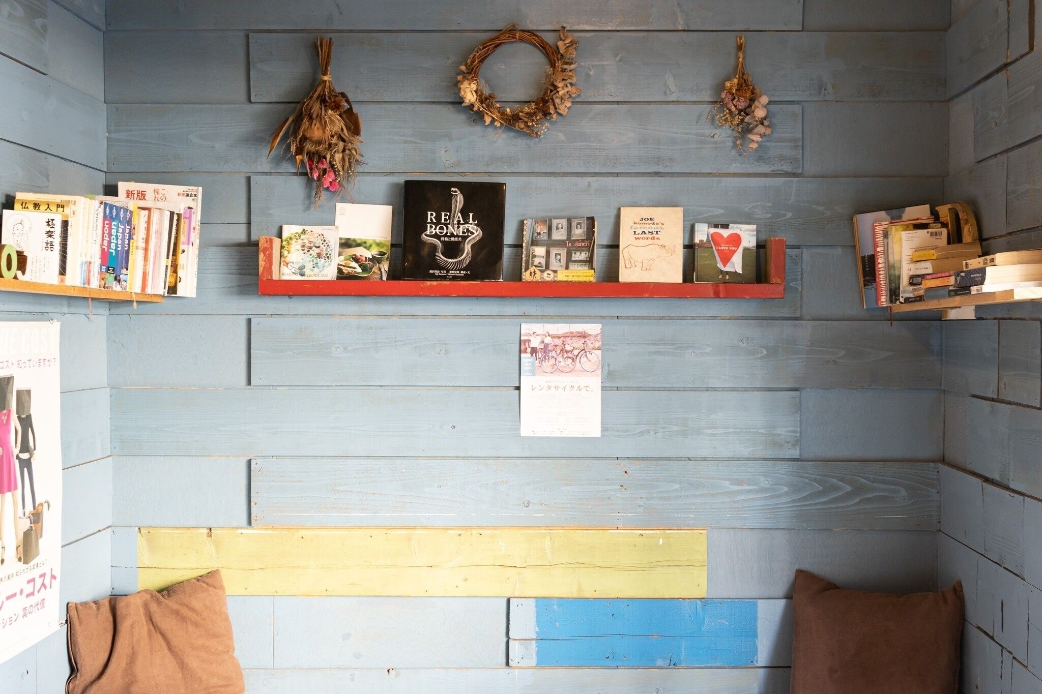 A room with a blue wooden wall, a bookshelf with books, a red shelf, and a yellow bench.
