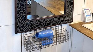 Un espejo con marco de mosaico, una mesa de madera y un secador azul en un estante.