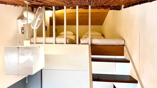 Una habitación compacta con una cama nido, un pequeño rincón de descanso y una escalera.