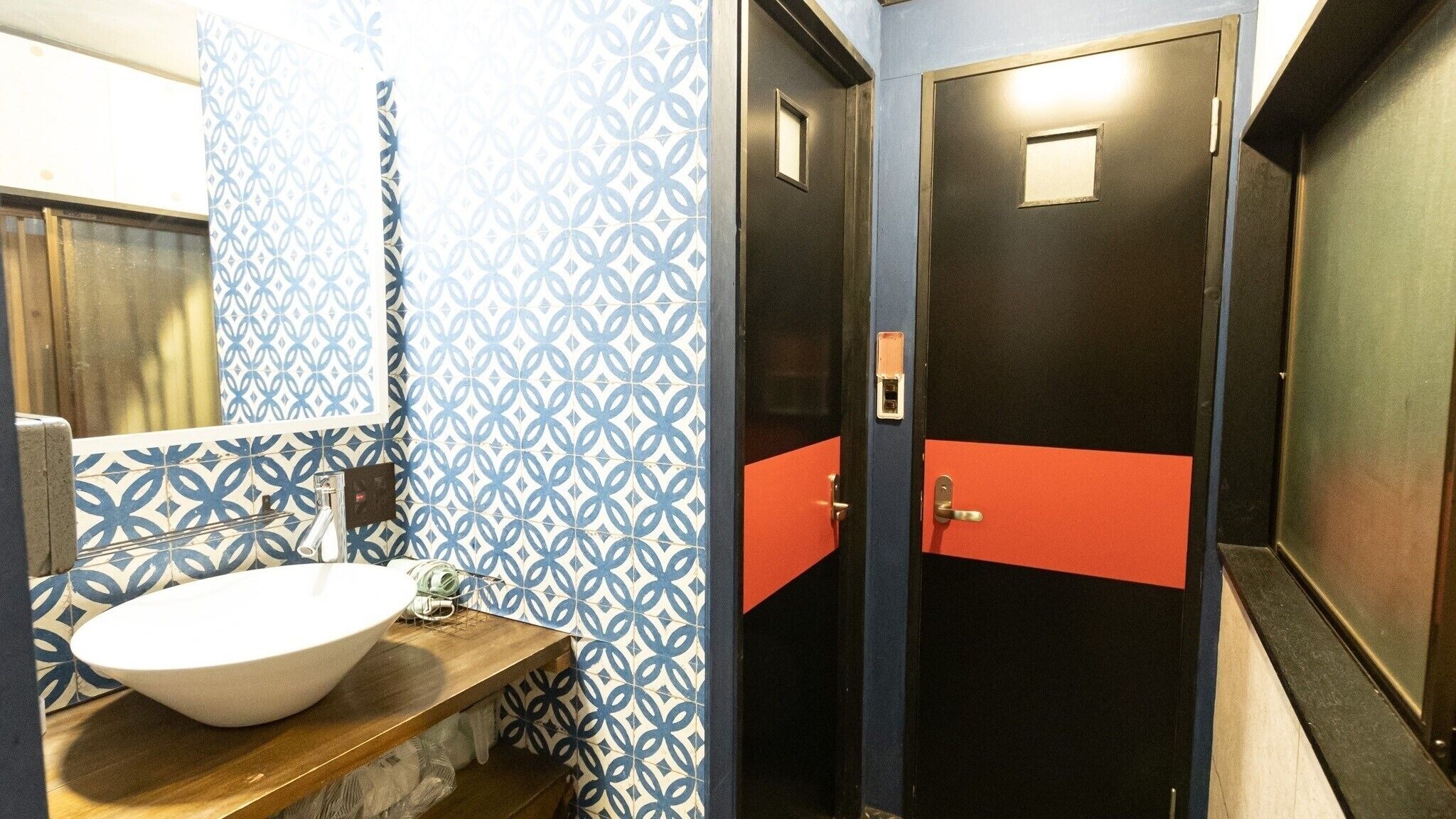 Ein Badezimmer mit einem gemusterten Wandbelag, einem weißen Waschbecken und zwei Türen mit roten Akzenten.