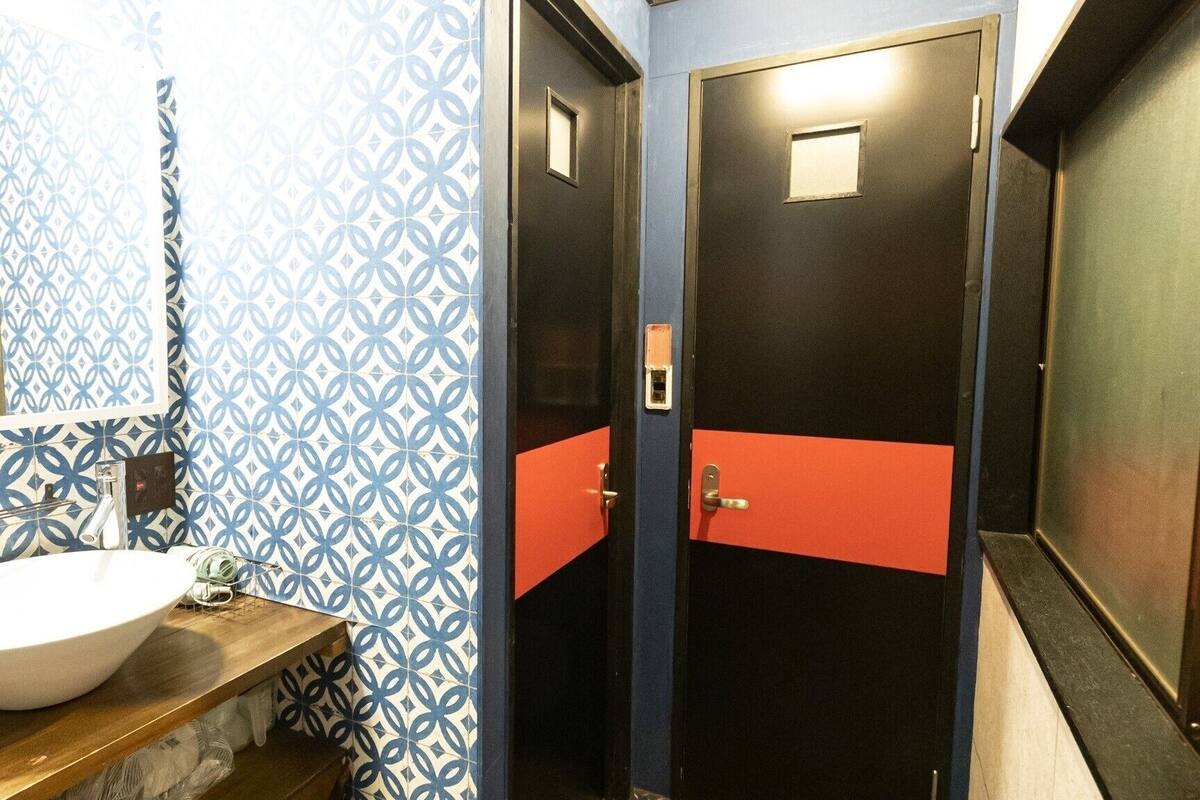 Un baño con pared estampada, un lavamanos blanco y dos puertas con detalles rojos.