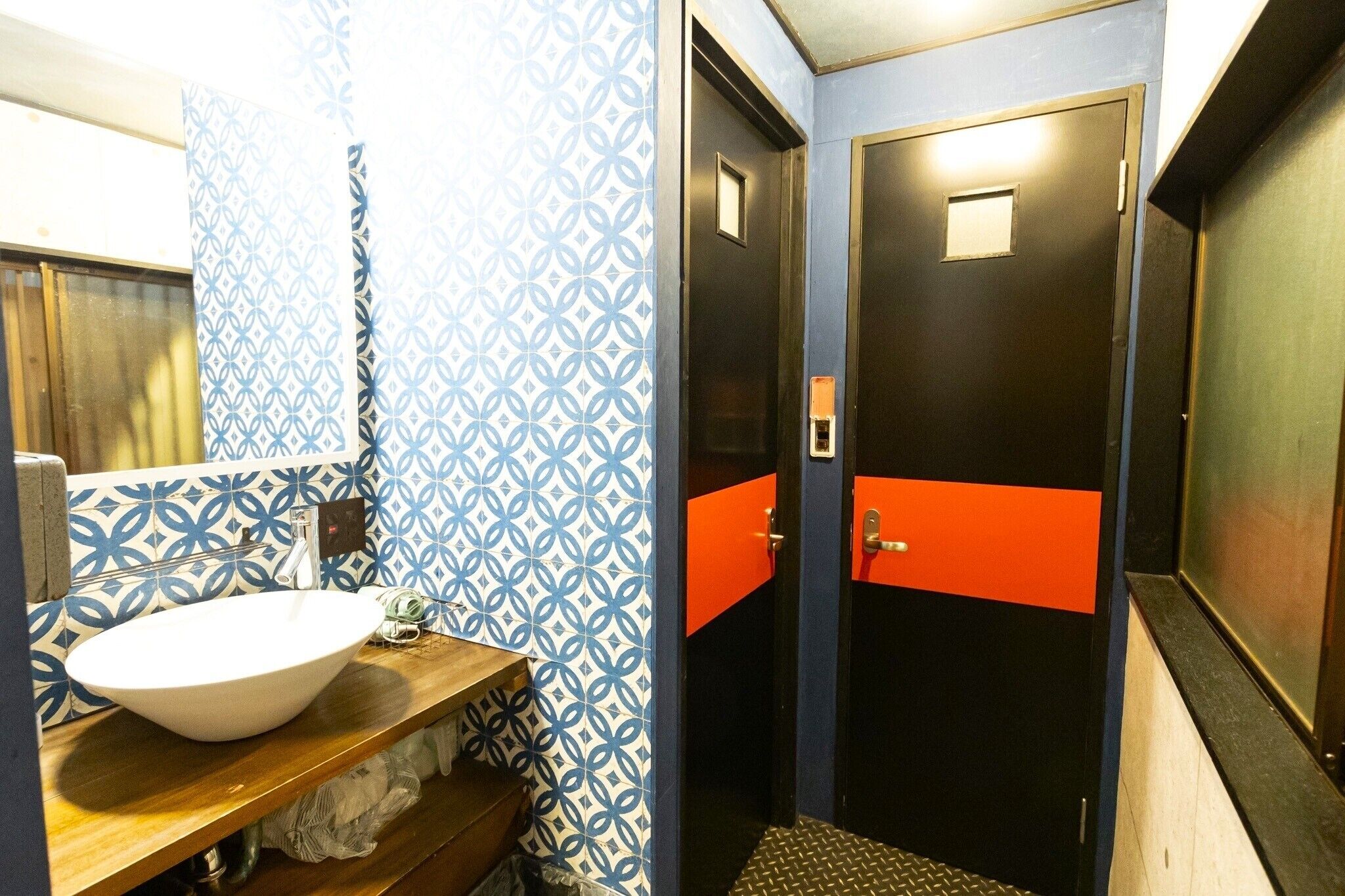 Un baño con un lavabo blanco, azulejos blancos y azules estampados, y una puerta roja.