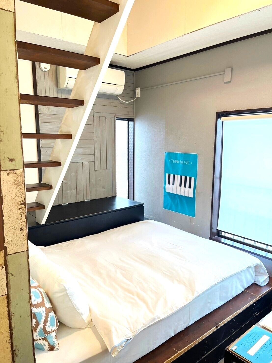 A bedroom with a bed, a window, a poster on the wall, and a staircase.