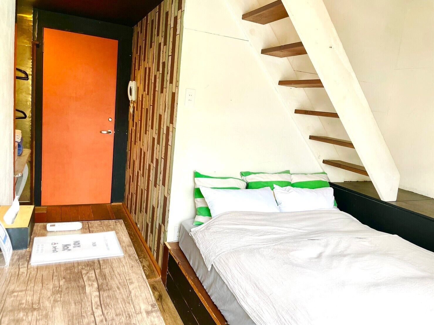 A bedroom with a bed, a wooden floor, a door, and a sloped ceiling.