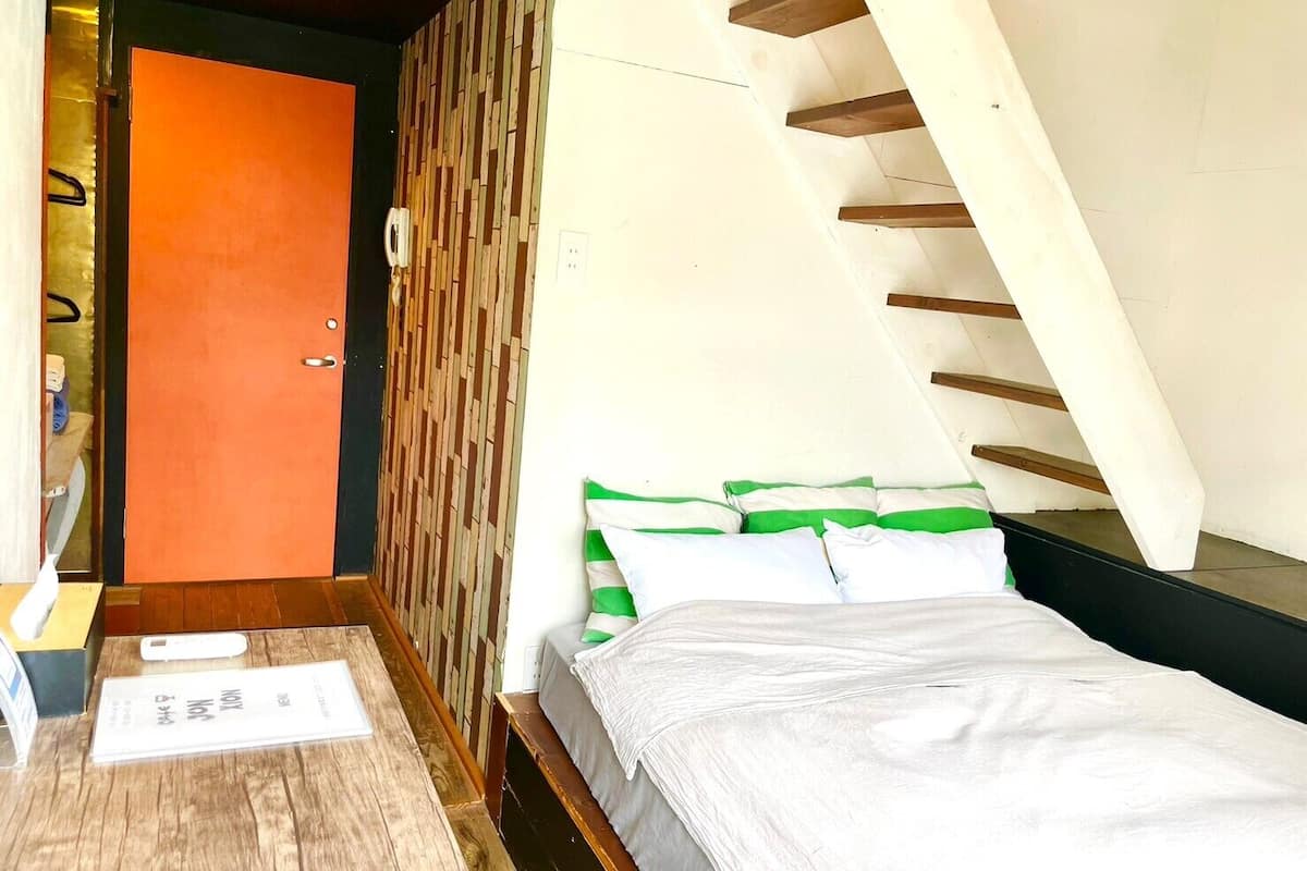 Un dormitorio con cama, suelo de madera, una puerta y techo inclinado.