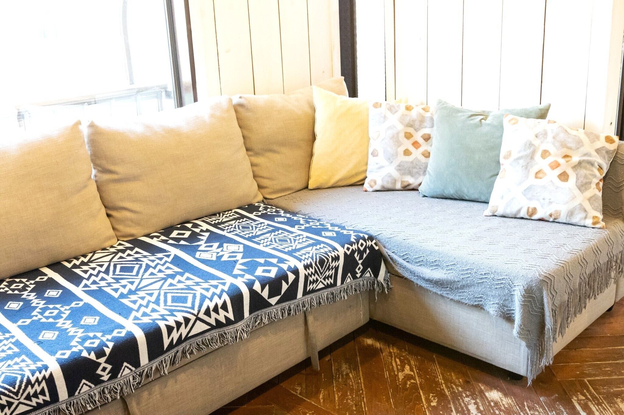A sectional sofa with patterned throw blankets and pillows in a room with wooden flooring.