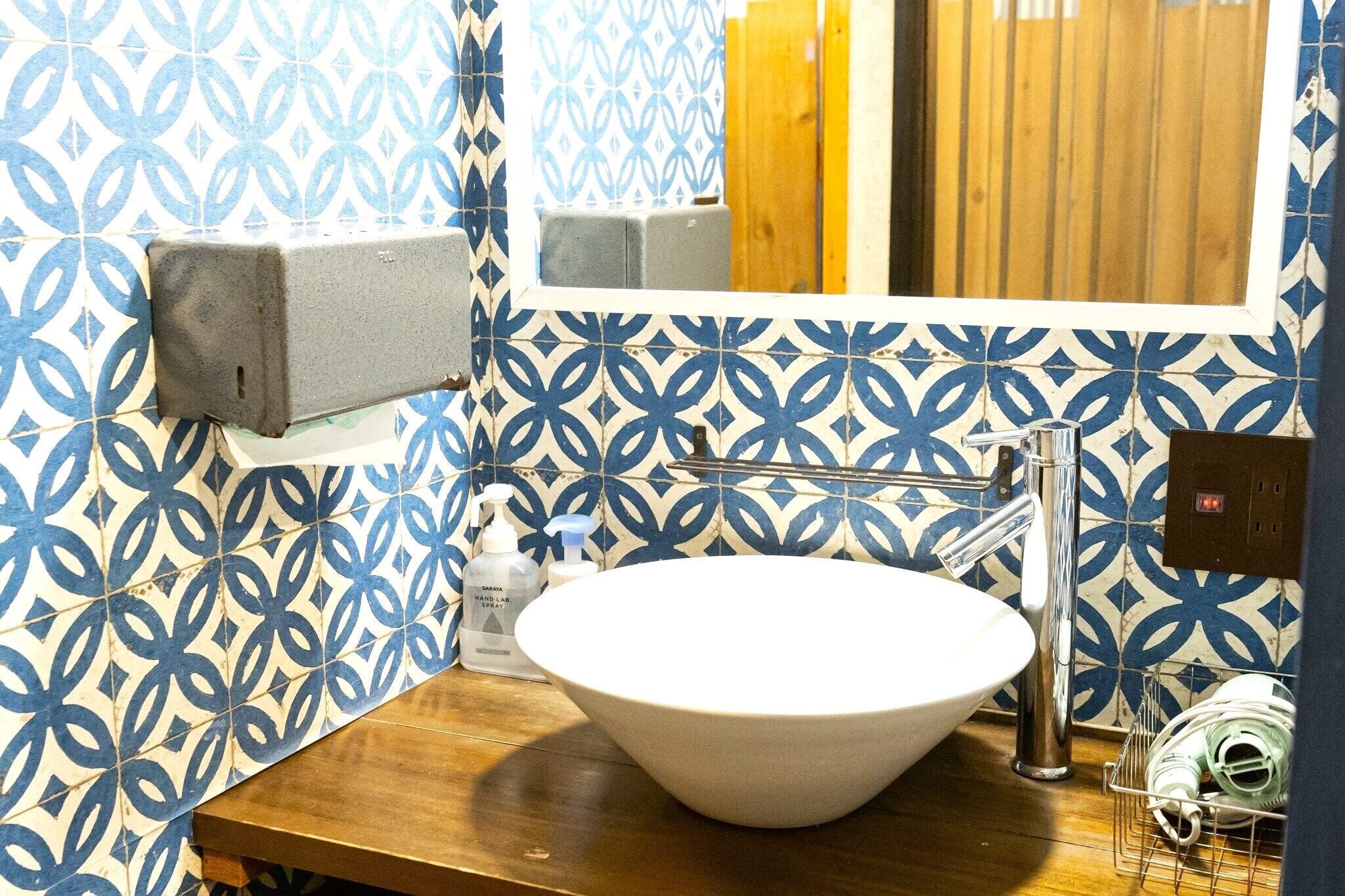 A bathroom with a white sink, blue patterned tiles, a hand sanitizer dispenser, and a mirror.