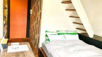 A bedroom with a wooden floor, a bed with white and green bedding, a wooden slatted ceiling, and a door with an orange panel.