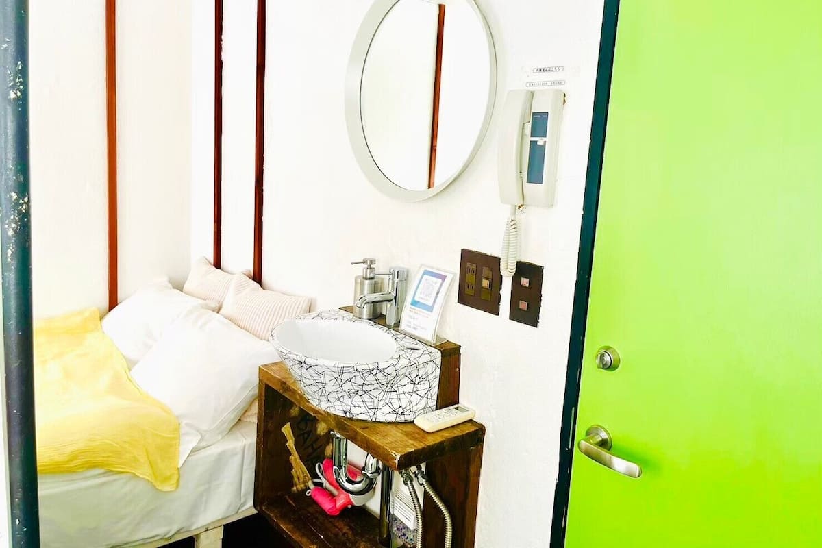 Una habitación de hotel con una cama, una mesita de noche con espejo, un teléfono y una puerta verde.