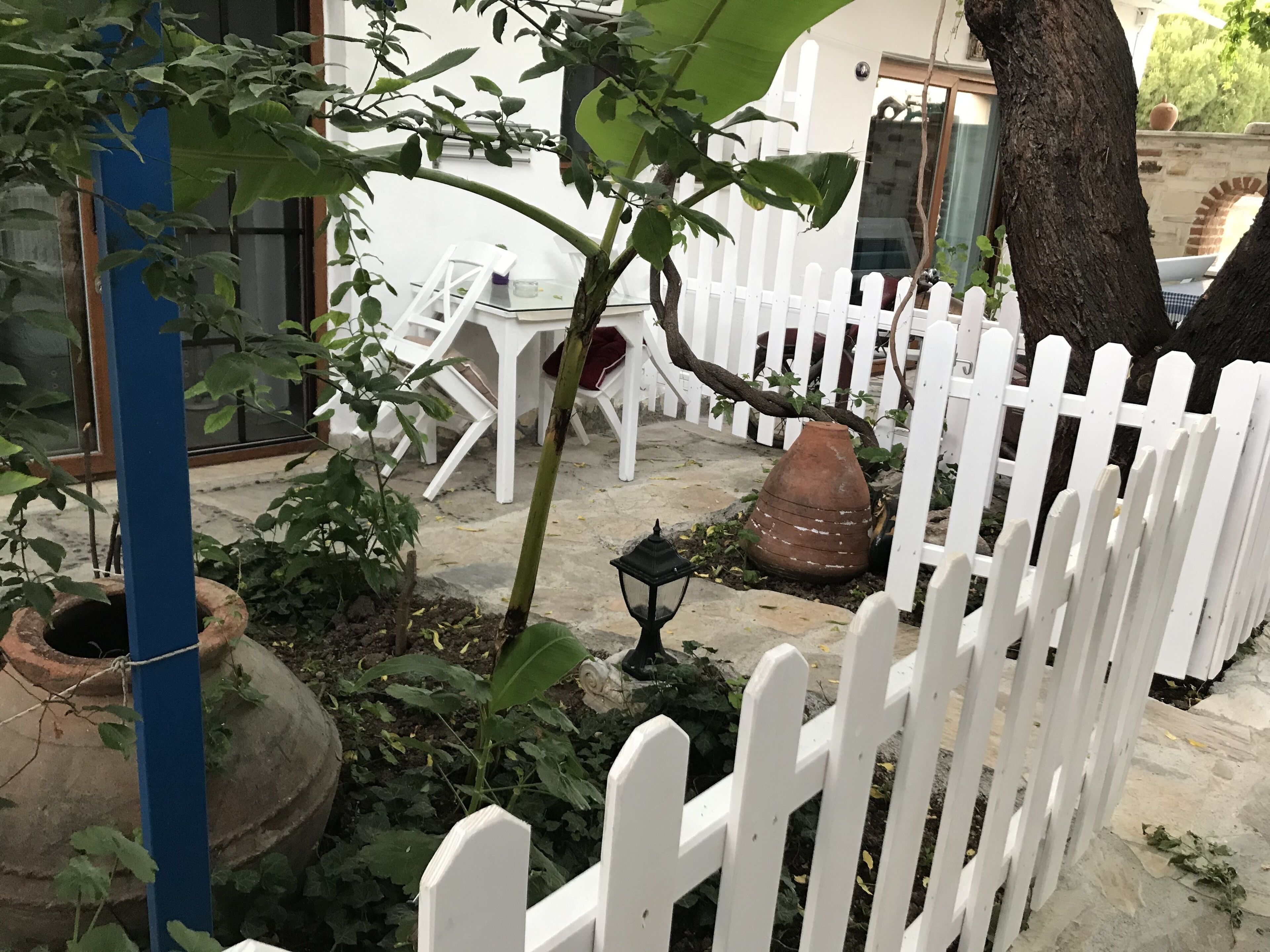 Een tuin met een witte schutting, bloempotten, een tafeltje en een stoel.