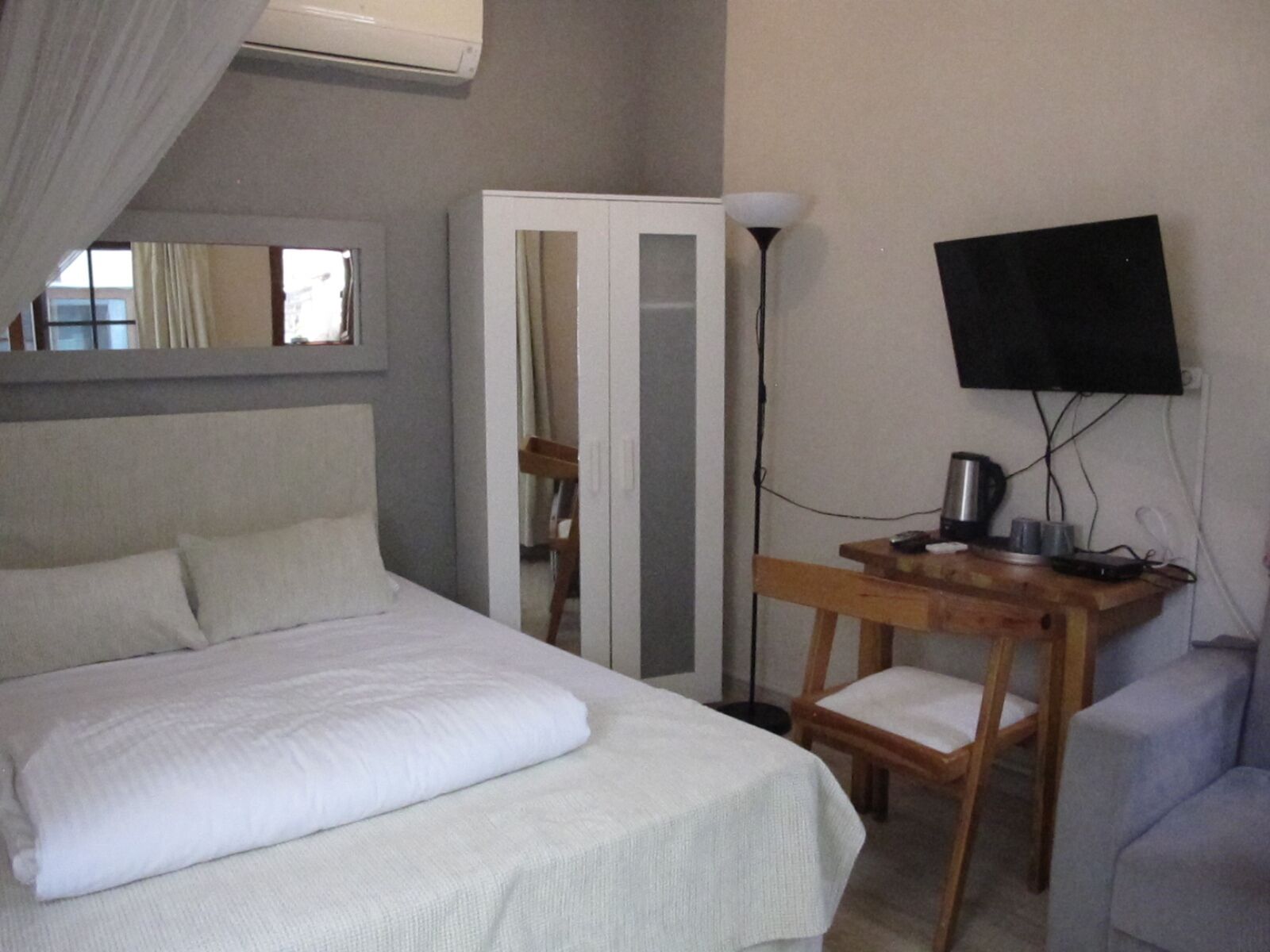 A bedroom with a bed, a desk, a chair, a wardrobe, a TV, and an air conditioning unit.