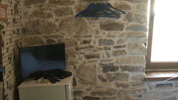 A room with a stone wall, a bed, a small desk with a computer, and a window with blinds.