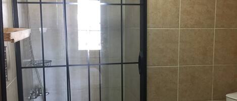 Ducha con cerramiento de vidrio y marco negro, inodoro y paredes de azulejos color beige.