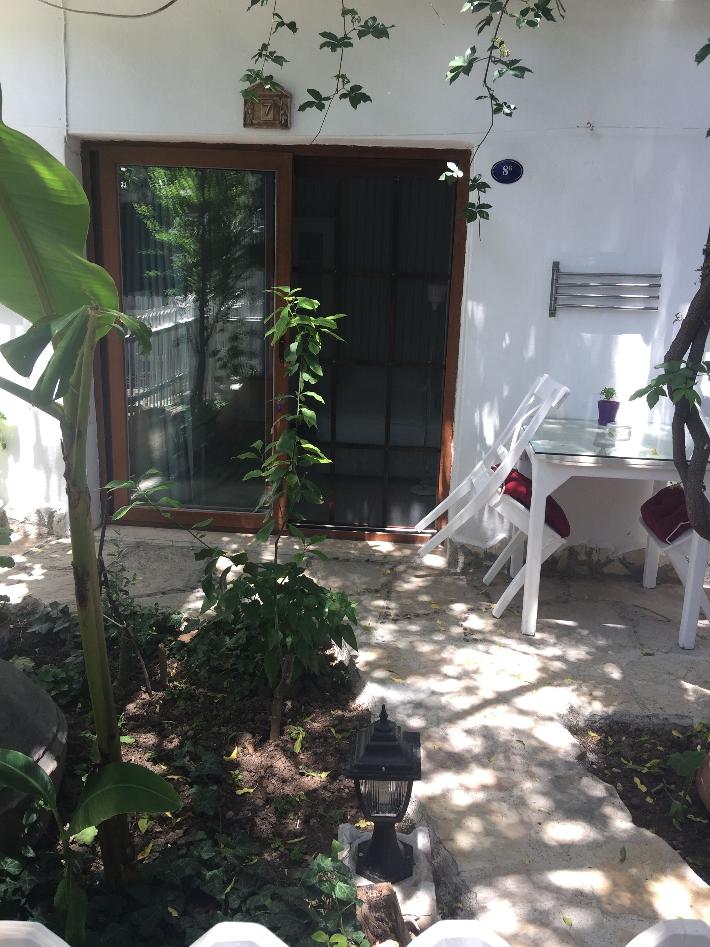A patio area with a glass door, white chairs, a small table, and a lantern.